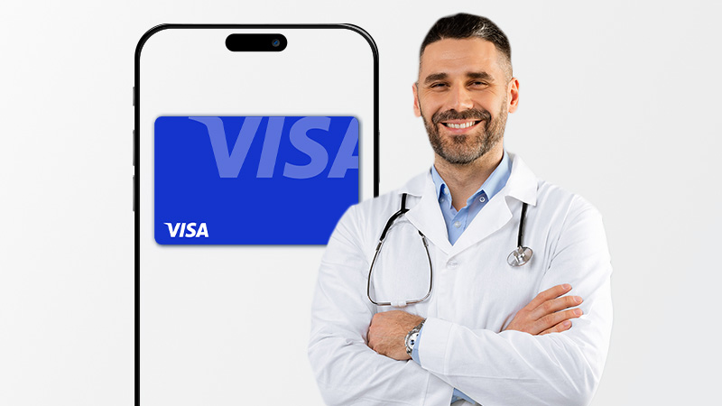 A smiling male doctor stands beside a smartphone displaying a blue Visa card on its screen.